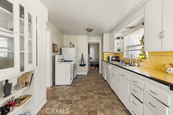 kitchen with white range with gas stovetop, a sink, white cabinetry, backsplash, and glass insert cabinets