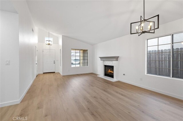 unfurnished living room with vaulted ceiling, light wood-type flooring, a fireplace, and baseboards