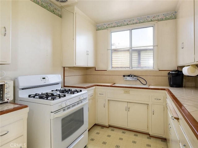 kitchen featuring tile countertops, light floors, tasteful backsplash, white cabinets, and white range with gas stovetop