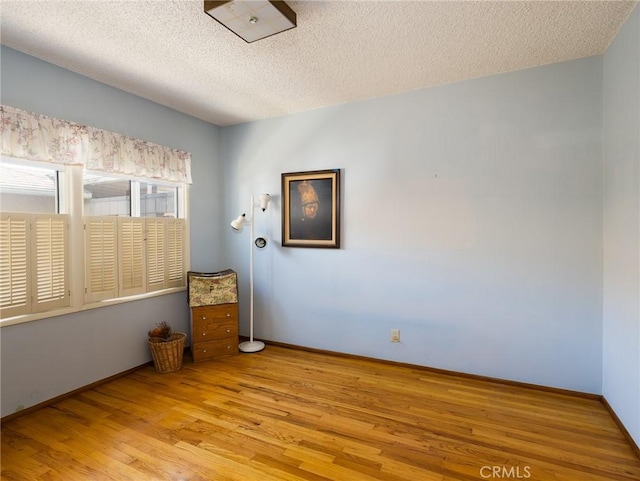 spare room featuring light wood-type flooring, a textured ceiling, and baseboards