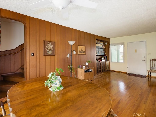 unfurnished dining area featuring wooden walls, ceiling fan, stairs, and wood finished floors