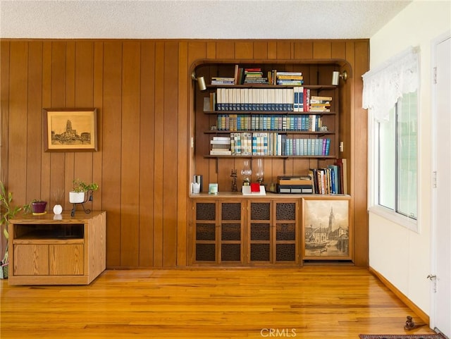 sitting room with light wood-type flooring, wood walls, and a textured ceiling