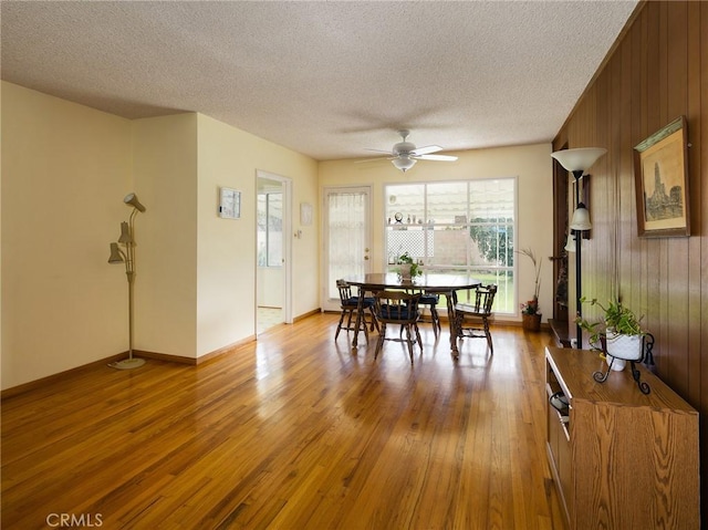 dining area with a textured ceiling, wooden walls, and light wood-style floors