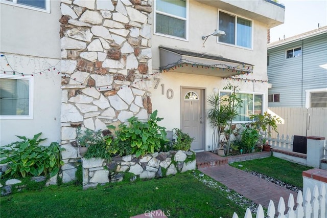 view of exterior entry with a lawn, fence, and stucco siding