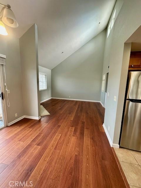 additional living space with light wood-type flooring, high vaulted ceiling, and baseboards