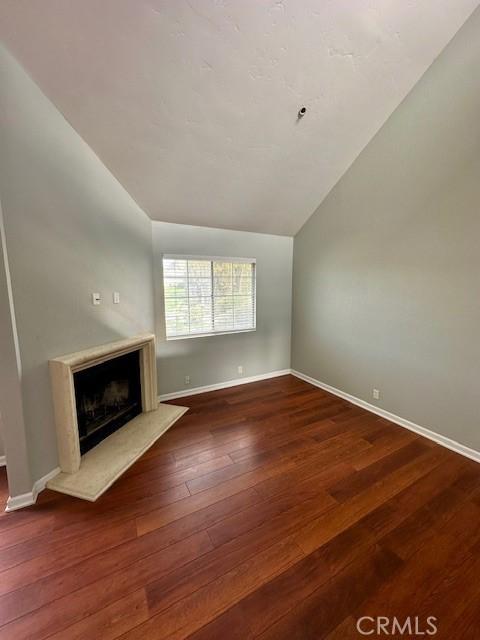 unfurnished living room with vaulted ceiling, a premium fireplace, dark wood-style flooring, and baseboards