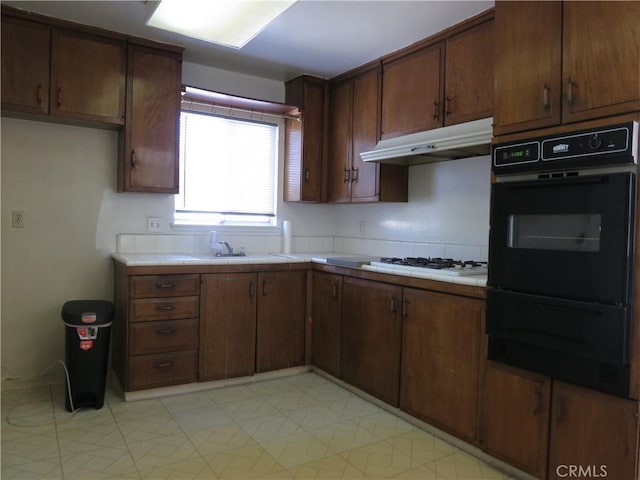 kitchen featuring dark brown cabinetry, dobule oven black, white gas stovetop, light countertops, and under cabinet range hood