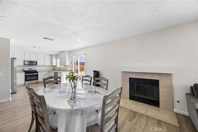 dining space featuring visible vents, baseboards, light wood-style floors, a textured ceiling, and a tiled fireplace