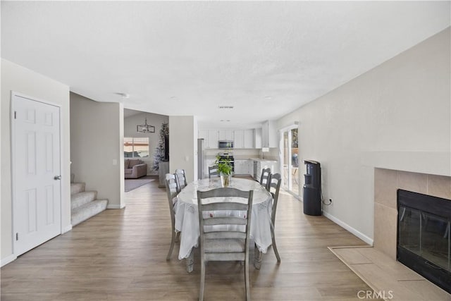 dining area with a fireplace, baseboards, stairs, and light wood-style floors