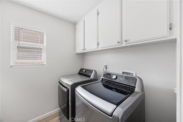 clothes washing area with light wood-type flooring, baseboards, cabinet space, and washer and clothes dryer