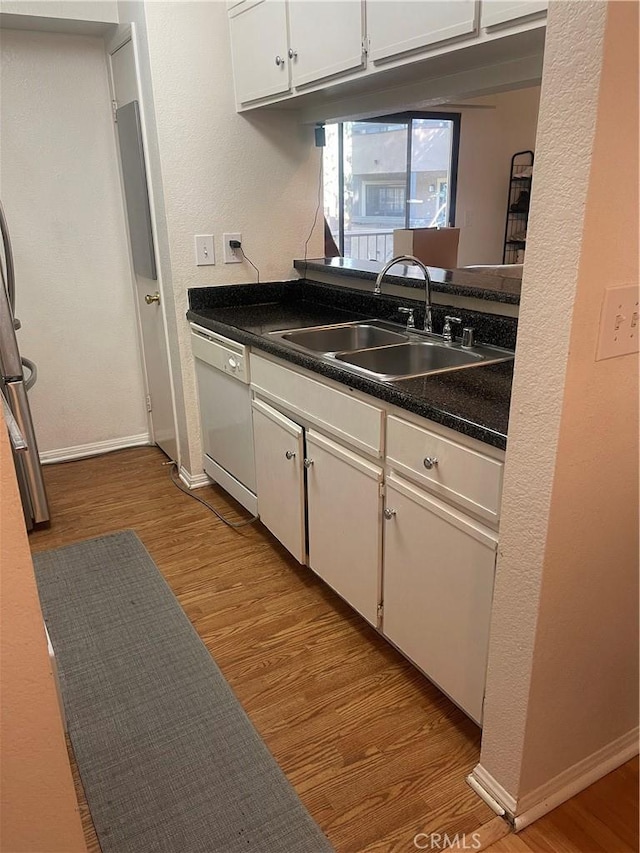 kitchen with baseboards, wood finished floors, white dishwasher, white cabinetry, and a sink