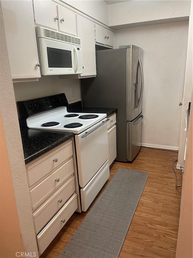 kitchen with dark wood finished floors, dark countertops, white cabinetry, white appliances, and baseboards