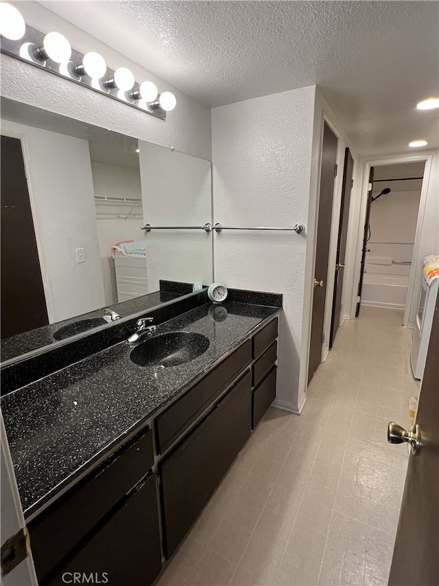 bathroom featuring a textured wall, tile patterned floors, a walk in closet, a textured ceiling, and vanity