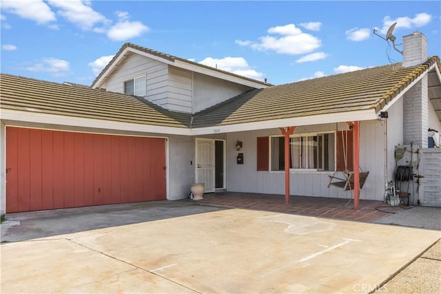 view of front of home with an attached garage, a tile roof, a chimney, and concrete driveway