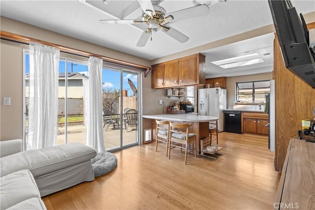 kitchen featuring black dishwasher, brown cabinetry, light wood-style floors, white fridge with ice dispenser, and a kitchen bar