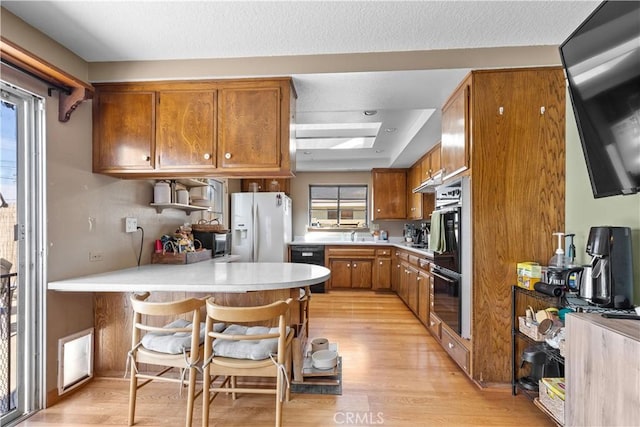 kitchen featuring brown cabinets, black appliances, light countertops, and light wood-style floors