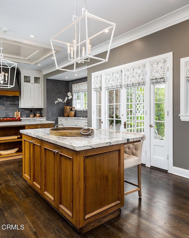 kitchen featuring a chandelier, light stone counters, a spacious island, brown cabinets, and pendant lighting