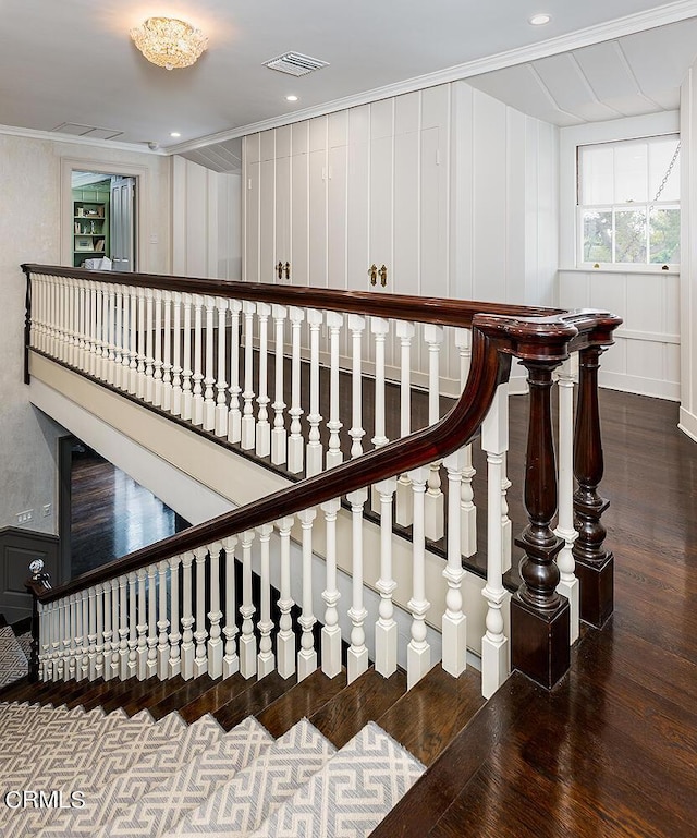 stairs with ornamental molding, visible vents, a decorative wall, and wood finished floors