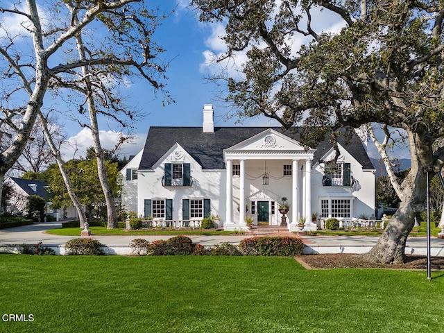 neoclassical home with a front yard, a chimney, and stucco siding