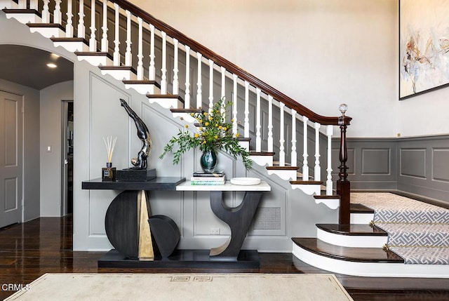 stairway featuring arched walkways, visible vents, a decorative wall, wainscoting, and wood finished floors