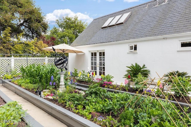 view of side of home with a shingled roof, a vegetable garden, fence, and stucco siding