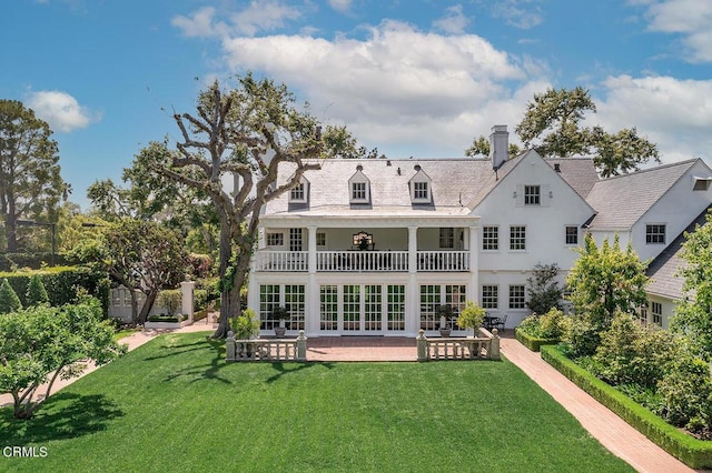 rear view of property featuring french doors, a balcony, a chimney, a yard, and a patio area