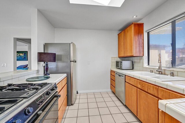 kitchen featuring a skylight, a sink, appliances with stainless steel finishes, tile counters, and tasteful backsplash