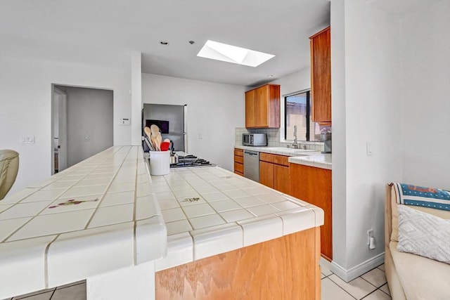 kitchen featuring a skylight, tile countertops, tasteful backsplash, appliances with stainless steel finishes, and a sink