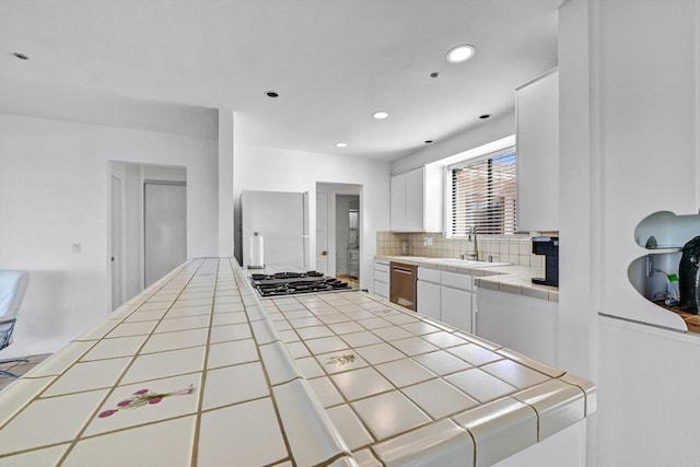 kitchen with tile countertops, a sink, white cabinetry, appliances with stainless steel finishes, and backsplash