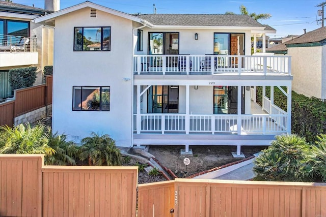 view of front of home with a porch, a fenced front yard, a balcony, and stucco siding