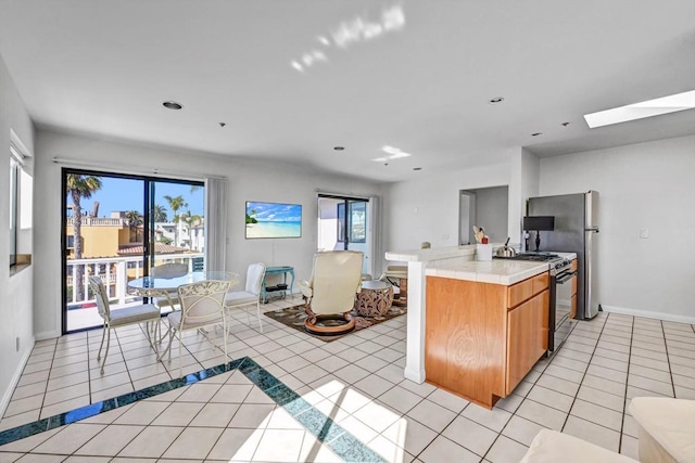 kitchen featuring light tile patterned flooring, a skylight, baseboards, light countertops, and black range