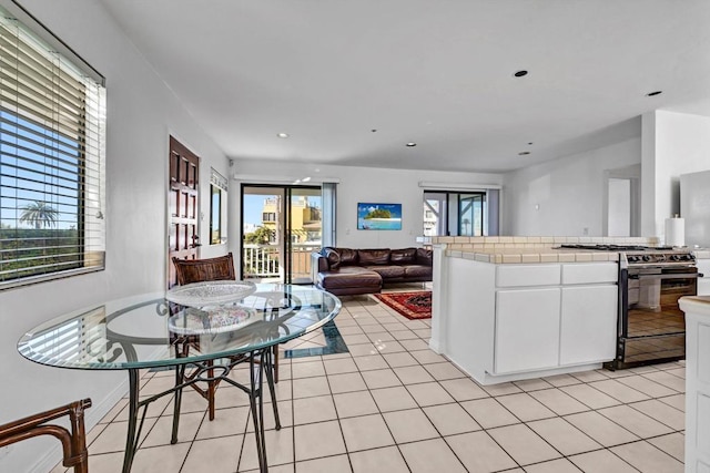 kitchen with light tile patterned floors, tile counters, gas range oven, open floor plan, and white cabinets