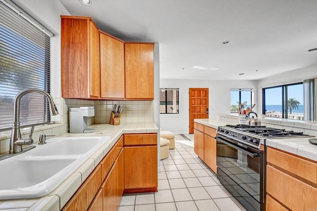 kitchen with tile countertops, black range with gas cooktop, light tile patterned floors, and a sink