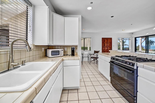 kitchen with light tile patterned floors, black range with gas cooktop, white microwave, a sink, and white cabinets