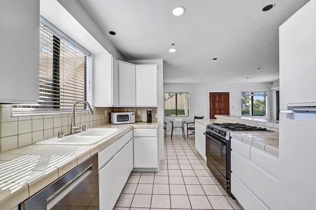 kitchen with black gas range, tile counters, and white cabinets