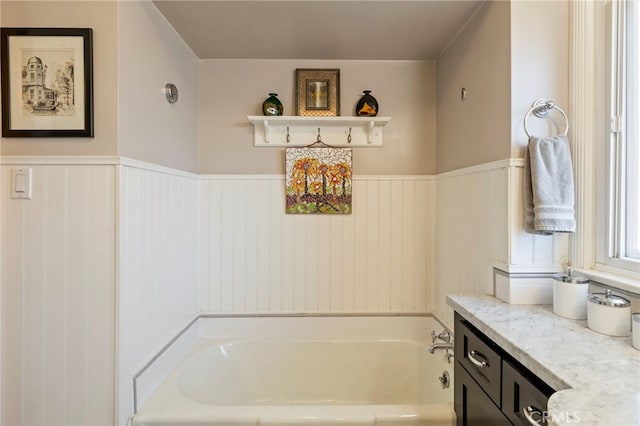 bathroom with a garden tub, wainscoting, and vanity