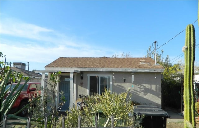 rear view of house featuring a shingled roof and stucco siding