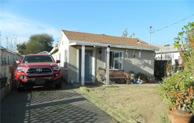 view of front of home featuring roof with shingles, fence, and stucco siding