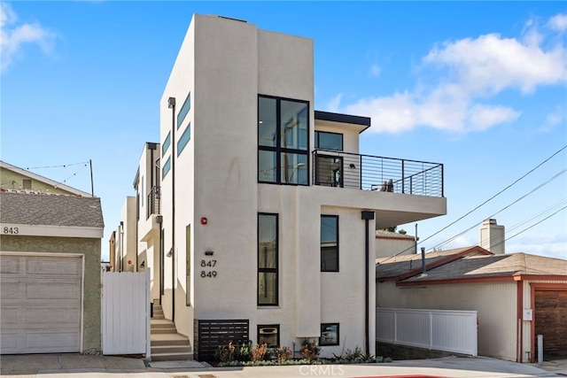 modern home featuring a garage, a balcony, fence, and stucco siding