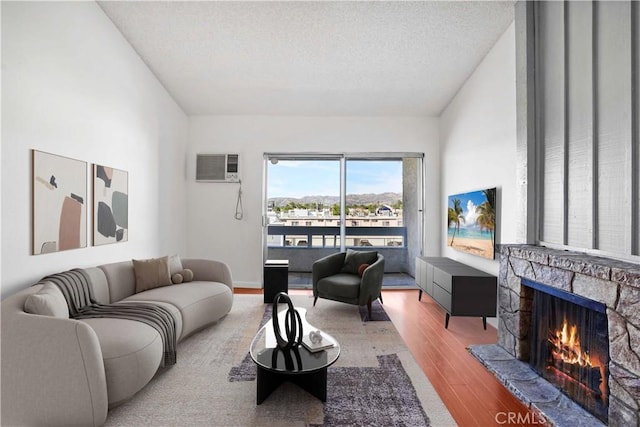 living room with a textured ceiling, a wall mounted AC, a fireplace, and wood finished floors