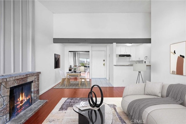 living room with a towering ceiling, a stone fireplace, baseboards, and wood finished floors