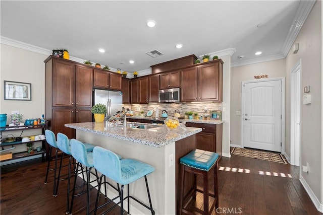 kitchen featuring crown molding, stainless steel appliances, visible vents, a kitchen island with sink, and a kitchen breakfast bar