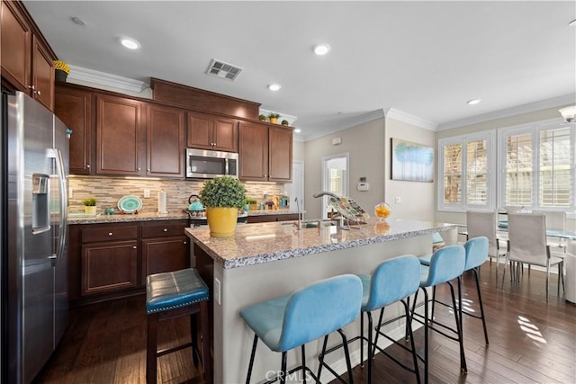 kitchen featuring a sink, visible vents, a kitchen breakfast bar, appliances with stainless steel finishes, and a center island with sink