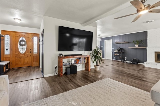 living room featuring beamed ceiling, a fireplace, dark wood finished floors, and visible vents