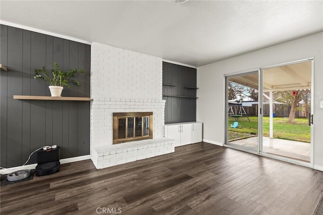 unfurnished living room with a brick fireplace, dark wood finished floors, and baseboards