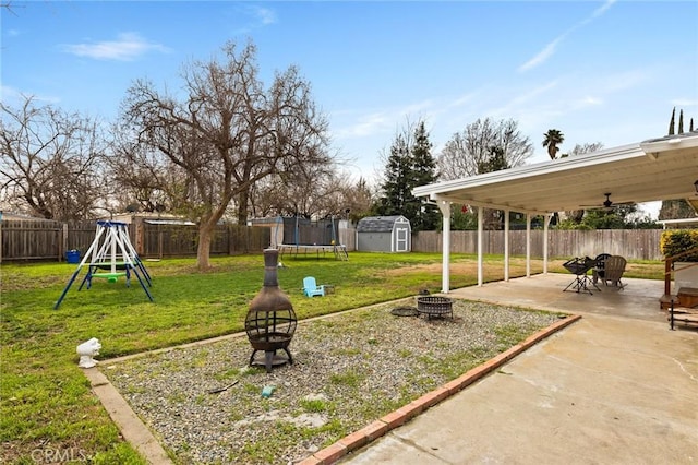 view of yard featuring an outdoor fire pit, a fenced backyard, a storage unit, a trampoline, and a patio area