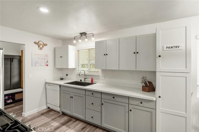 kitchen featuring light countertops, gray cabinetry, a sink, light wood-type flooring, and dishwasher