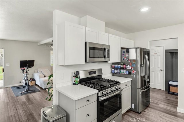 kitchen with stainless steel appliances, wood finished floors, light countertops, and white cabinets