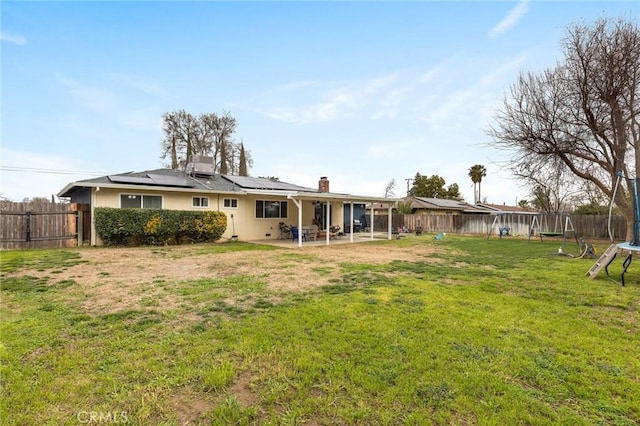 back of property featuring a patio, a fenced backyard, solar panels, a yard, and a trampoline