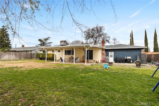 back of house featuring an outdoor fire pit, a fenced backyard, a lawn, and stucco siding